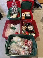 Five plastic tubs filled with assorted Christmas ornaments and supplies including tree toppers, ribbons, and boxed light set.