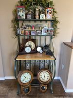 Full view of the metal baker's rack holding multiple vintage clocks and collectible tins with colorful vintage advertising, including Coca-Cola tins and various small clocks placed on shelves and tabletop.
