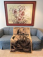 Floral painting and sailing ship reel matte displayed on a blue couch showing relative size.