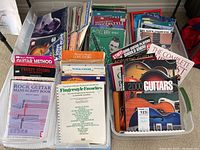 Large bins filled with a variety of guitar instruction and music books, along with sheets of music manuscript paper.