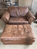Front view of brown leather chair with matching ottoman showing seating surfaces and brass brad trim