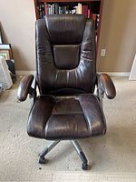 Front view of brown leather office chair showing padded seat, backrest with inset cushion, padded armrests and swivel base with wheels.