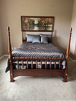 Front view of wood pineapple 4 poster queen bed with bedding and mattress visible underneath. Shows bed in assembled state with details of posts and frame.