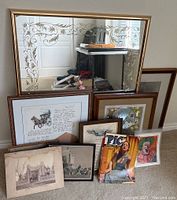 Photo showing large ornate gold-tone framed mirror with etched floral decoration, leaning against wall over framed prints and magazine.
