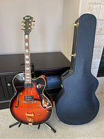 Full view of guitar on stand alongside closed hard case in room