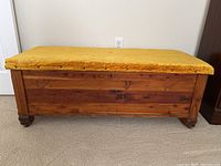 Front view of the cedar chest showing yellow velvet cushioned top and wooden body with carved feet.