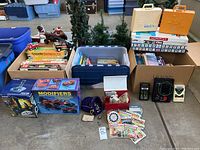 Wide angle showing all tubs, board games boxes stacked, toys, and electronic kits arranged on concrete floor