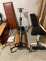 View showing brown padded bench, Nordic Track machine, and black bench frame parts in basement area.