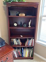 Front view of the wood bookcase showing five shelves with minor wear and various items on shelves.