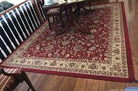 Full view of the red Kashan design area rug under a dining table showing general condition and pattern.
