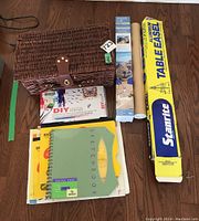 Photo showing the full lot contents including the boxed Starlite aluminum table easel, rolled poster, multiple sketchbooks, a DIY DIY book, and a woven basket likely containing art materials.