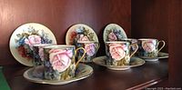 Six demitasse cups and saucers with pink rose floral design arranged on wooden shelf