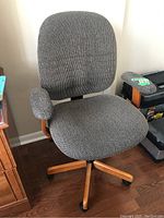 Front and side view of an upholstered office chair with wood veneer frame, caster wheels, and padded armrests in a textured gray fabric.