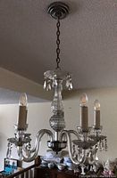 Full view of the vintage glass chandelier showing candle-style lights with hanging crystal drops and central glass column, mounted on ceiling with chain.
