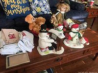 Wide view of entire Christmas and holiday decor lot on wooden coffee table showing snowmen, dolls, teddy bears, towels, basket.