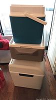 Stack of three coolers: teal Rubbermaid cooler with beige handle on top, brown Coleman Party Stacker cooler in middle, white Koolatron plug-in cooler on bottom.