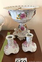 Photo of the two Dresden porcelain candle holders and pedestal bowl with floral 3D decorations and gold trim on a wooden surface
