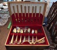 Open Community Plate box displaying gold toned Lifetime stainless flatware arranged with knives in back slot, forks and spoons in front sections, showing handles with textured ornate pattern.