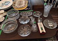 Full display of the lot on a table showing various glass and crystal bowls, candle holders, divided dishes, salt and pepper shakers, and the Mikasa bottle stopper box.