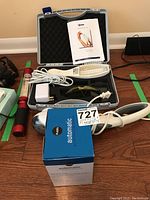 Display of the blood pressure monitor box, massager device with carrying case and manual, Dermfix UV comb, and wand light on wooden floor.