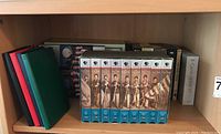 Shelf with assorted media sets and empty journals visible, including The Civil War VHS set in blue cases, four hardcover journals in red, green, blue, and black, and boxed media sets behind them.