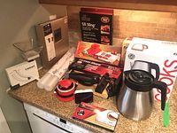 Photo showing multiple kitchen items including white Cuisinart scale, various kitchen tools, and Cooks electric kettle box.
