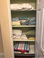 Full view of linen closet shelves with stacked linens including sheets, towels, and duvet.
