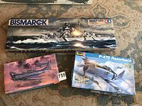 Three model kit boxes displayed on carpet: Tamiya Bismarck battleship, Hasegawa SBD-3 Dauntless, and Revell P-47D Razorback