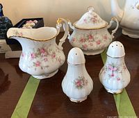 Full set photo showing creamer, sugar bowl with lid, salt and pepper shakers on a table