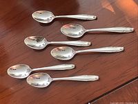 Set of six sterling silver demitasse spoons arranged on a wooden surface, showing the front side and decorative handles.