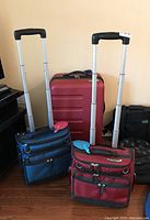 Photo showing all three suitcases standing upright with extended handles: red Swiss Gear hardcase in the back and the two smaller Magellans carry-ons in front (red and blue).