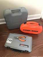 Three closed tool cases including a gray Sears Craftsman, orange Black & Decker, and a large gray Kawasaki case with pliers on top.
