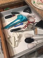 Photo of kitchen utensils in drawer showing ladles, spatulas, peelers, measuring spoons, a strainer, and whisks.