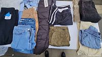 A mixed assortment of men's and women's pants including denim, corduroy, swim trunks, and snow pants arranged on a white background.