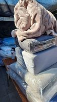 Stack of packaged gray chair cushions with a folded plush blanket on top.