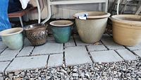 Five ceramic planter pots arranged on stone tiles outdoors, showing different sizes, colors and styles.