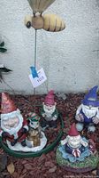 Overall lot showing garden gnomes arranged around large bee garden spike stuck in soil with mulch.