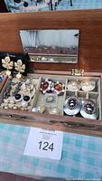 Wooden jewelry box open showing interior mirror and assorted vintage earrings arranged inside