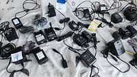 Wide view of collection showing multiple power cords, USB adapters, and chargers spread on a surface with labels.