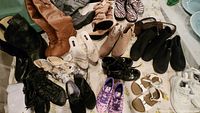 Photo showing a collection of various kids and adult footwear laid out on a surface including boots, sandals, dress shoes, and sneakers.