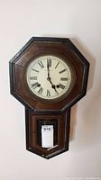 Front view of antique wooden wall clock with octagonal face and Roman numerals, showing clock hands and outer wooden frame.