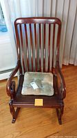 Front view of the antique wooden rocking chair with cushion on the seat and vertical slats on the backrest.