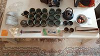 Wide shot of tea sets, ceramic cups, bowls, teapot, spoons, napkin holders, chopsticks, and plates displayed on table.