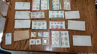 Overhead photo showing multiple uncirculated and proof coin sets from the 1960s to 1981 with original packaging and envelopes on a woodgrain table