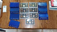 Wide view of all three proof coin sets and their blue cardboard boxes on a wooden table.