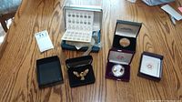 Overview shot of all four items on wooden table: presidential coin folder, bicentennial medal box, silver eagle coin box, eagle pin box