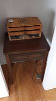 Wooden DMC branded storage box on top of a dark wooden Kenmore sewing table, closed drawers visible