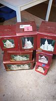 Overview of all seven red Village Treasures boxes including bank, churches, train station and carousel