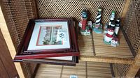 Photo showing three framed lighthouse prints stacked and four painted lighthouse figurines on a woven shelf.