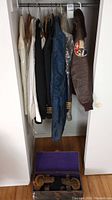 Closet view showing hanging garments: white dress jacket, white naval jacket, black tuxedo jacket, blue jacket, brown leather flight jacket with patch